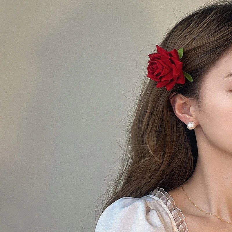 Femme brune aux longs cheveux lachés coiffée d'une pince à cheveux en forme de rose de couleur rouge.